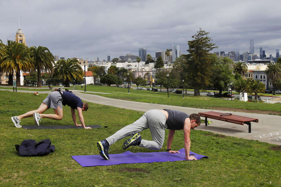 FILE: San Franciscans keep their distance for coronavirus concerns while using a phone app to do a full body weight workout at Mission Dolores Park. Gyms can begin reopening starting Friday. Photo: Jeff Chiu/Associated Press