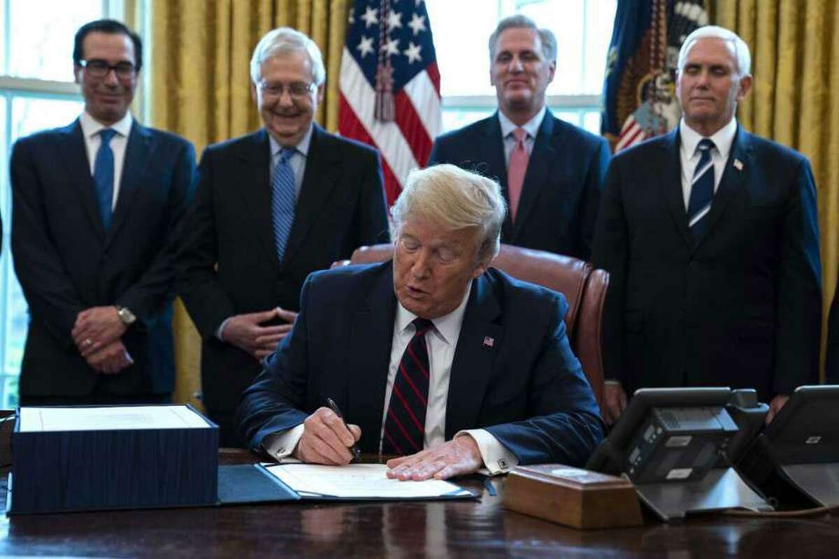 FILE - In this March 27, 2020 file photo, President Donald Trump signs the coronavirus stimulus relief package in the Oval Office at the White House in Washington, as Treasury Secretary Steven Mnuchin, Senate Majority Leader Mitch McConnell, R-Ky., House Minority Leader Kevin McCarty, R-Calif., and Vice President Mike Pence watch. Payments from a federal coronavirus relief package could take several weeks to arrive.
