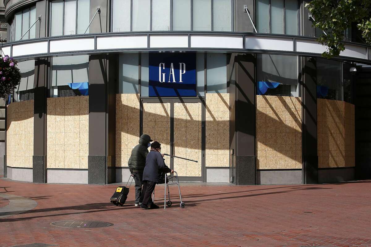 2020年3月27日星期五，加利福尼亚州旧金山，戴着口罩的行人走过鲍威尔街和市场街的Gap商店。Gap将永久关闭其在市场街的旗舰店，以及旧金山的另外两家商店。