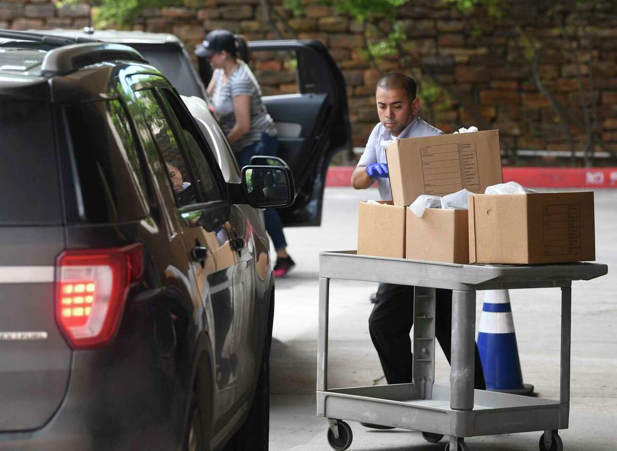 Joe Vidales pulls a cart loaded with groceries and meals to load into an employee’s vehicle at USAA’s headquarters on Tuesday. The curbside meal and grocery pickup for employees is a new program to help workers dealing with the pandemic.