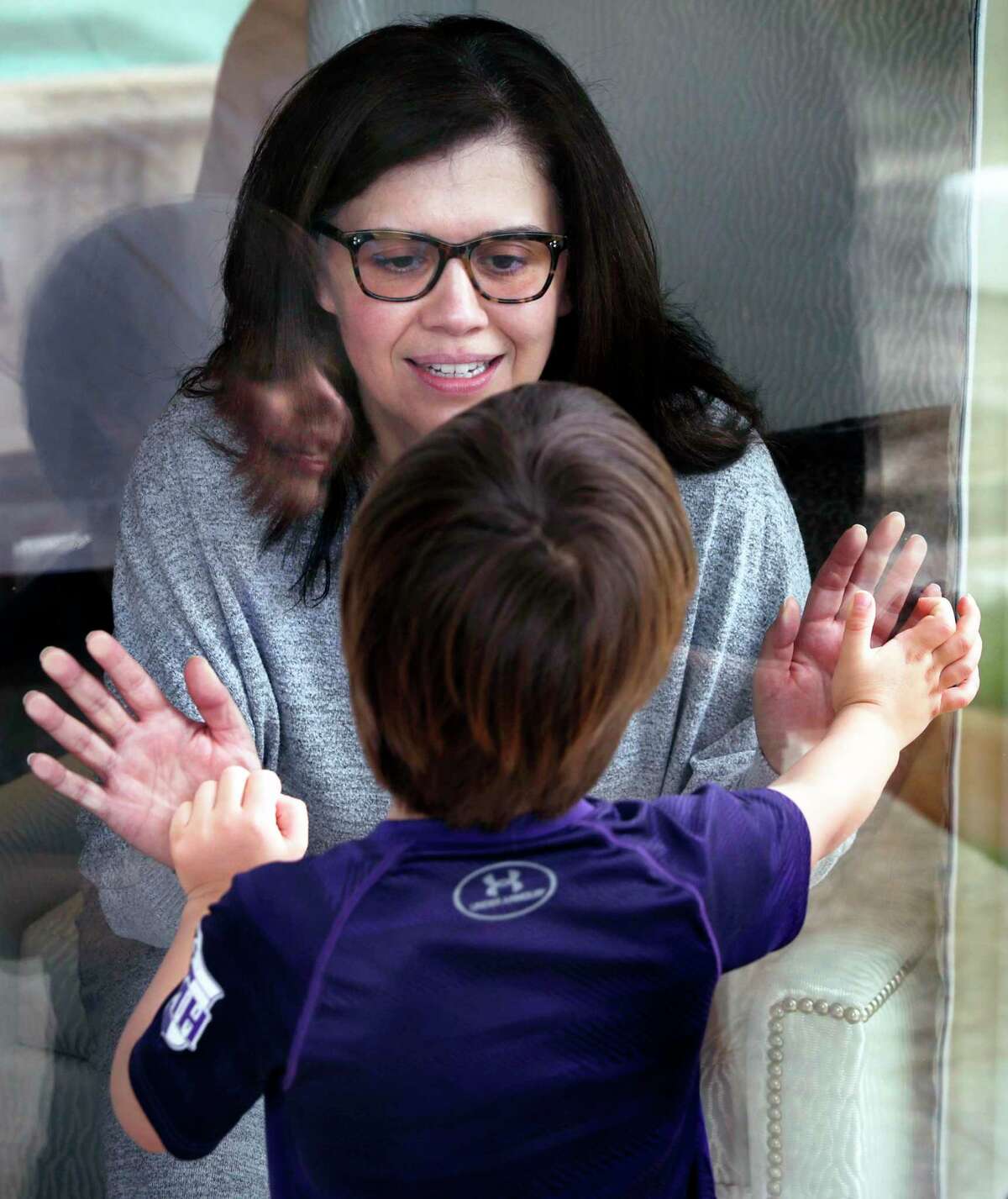 Justice Luz Elena Chapa greets her son Jose Chapa, 5, through a glass door. Chapa, Justice of the 4th Court of Appeals was infected with the new coronavirus on a trip to Utah over Spring Break, on Monday, March 30, 2020.