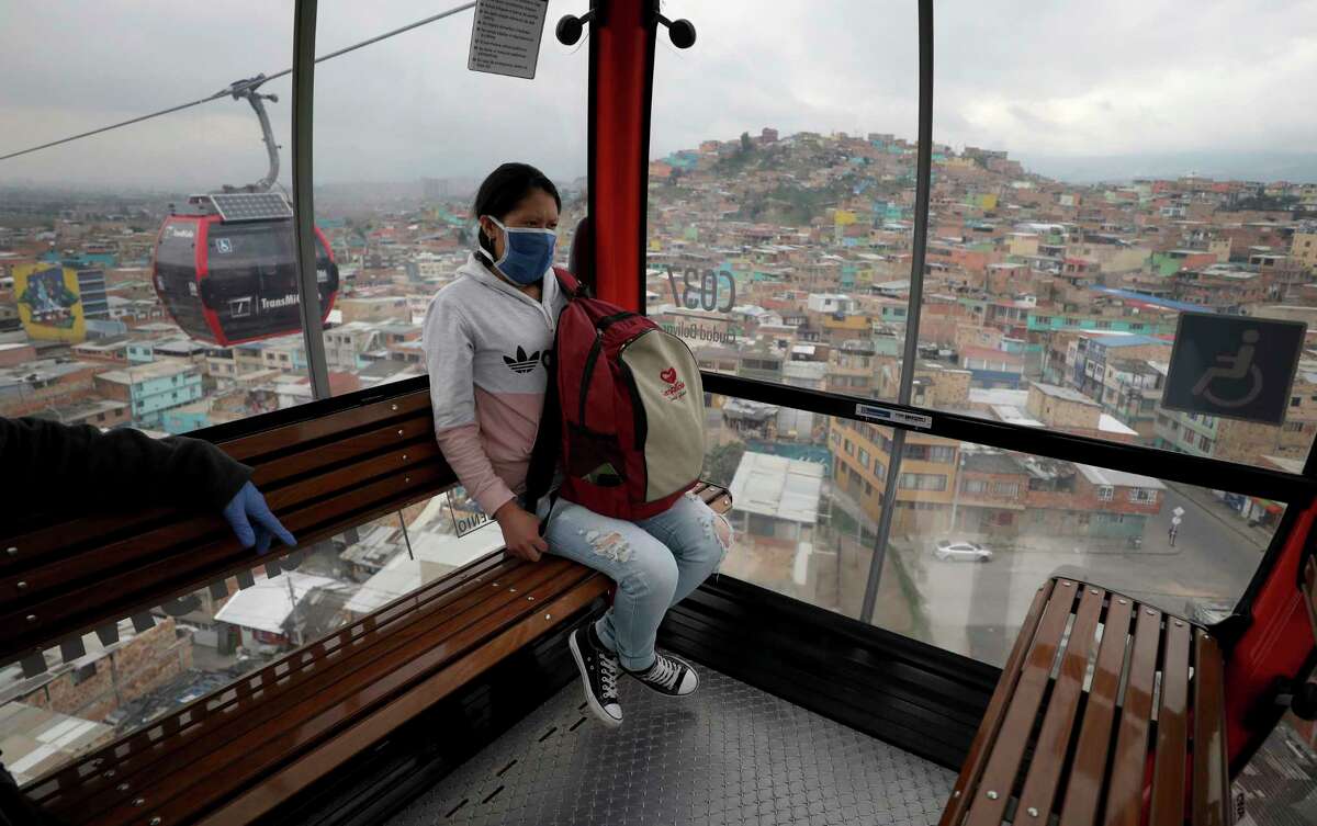 A woman, wearing a protective face mask as a precaution against the new coronavirus, rides in a public cable car in Bogota, Colombia, Wednesday, April 1, 2020. Health authorities have begun checking the temperature of commuters as a measure to contain the spread of COVID-19.
