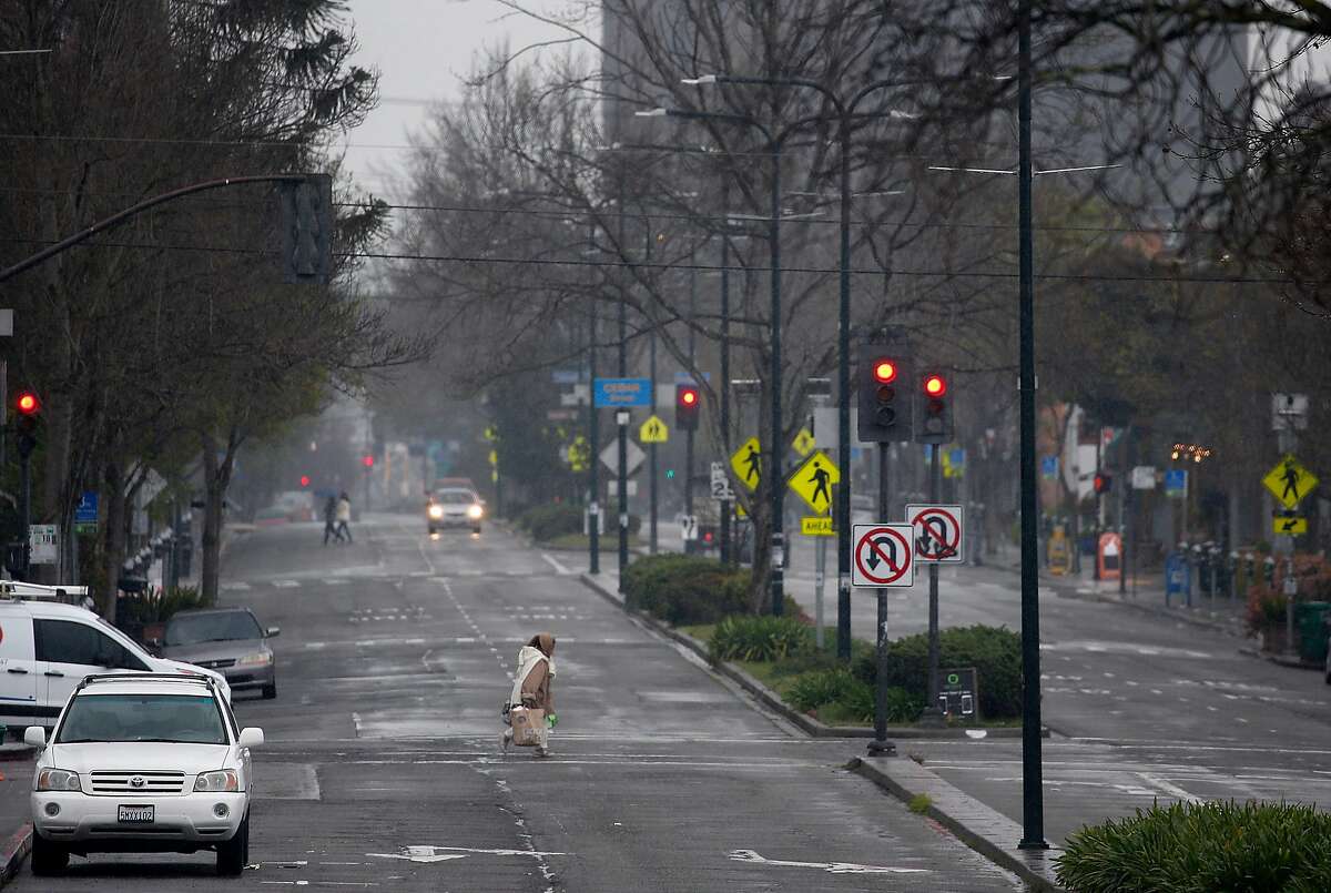 A woman crosses Shattuck Avenue which is normally filled with traffic in Berkeley, Calif. on Saturday, March 28, 2020. Air quality has improved significantly as fewer vehicles are on the streets and highways while shelter in place orders remain in effect during the coronavirus pandemic.