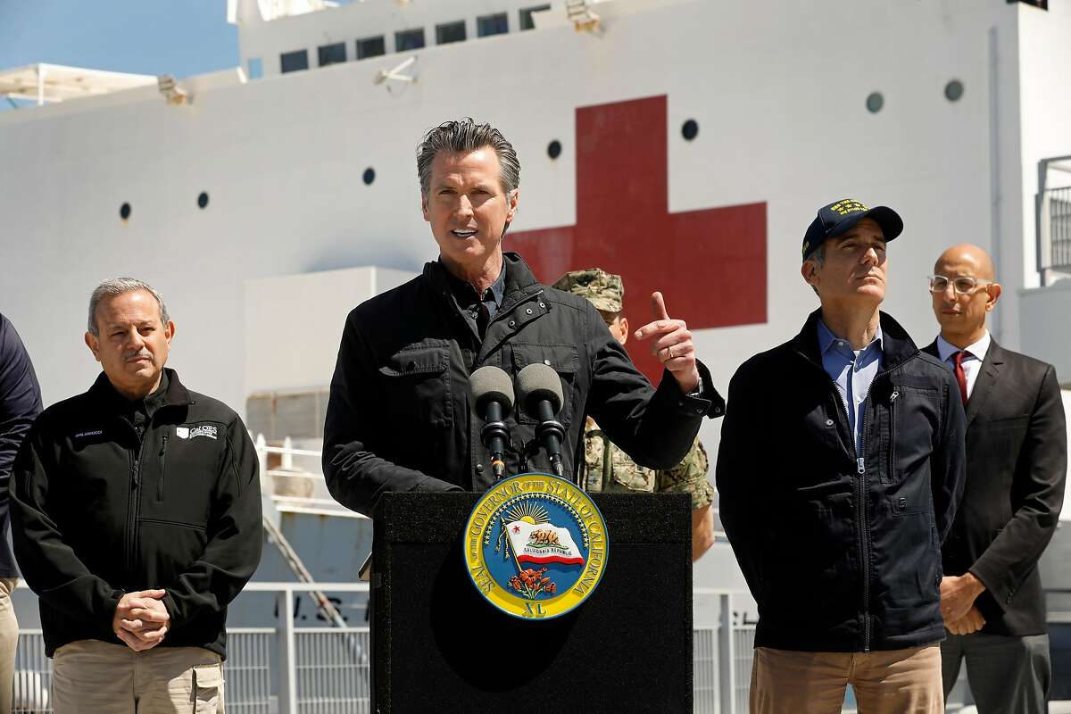 LOS ANGELES, CALIFORNIA-MARCH 27, 2020-California Governor Gavin Newsom speaks in front of the hospital ship USNS Mercy that arrived into the Port of Los Angeles on Friday, March 27, 2020, to provide relief for Southland hospitals overwhelmed by the coronavirus pandemic. Also attending the press conference were Director Mark Ghilarducci, Cal OES, left, Los Angeles Mayor Eric Garcetti, second from right, and Dr. Mark Ghaly, Secretary of Health and Human Services, far right, along with others not shown. (Carolyn Cole/Los Angeles Times/POOL/TNS)