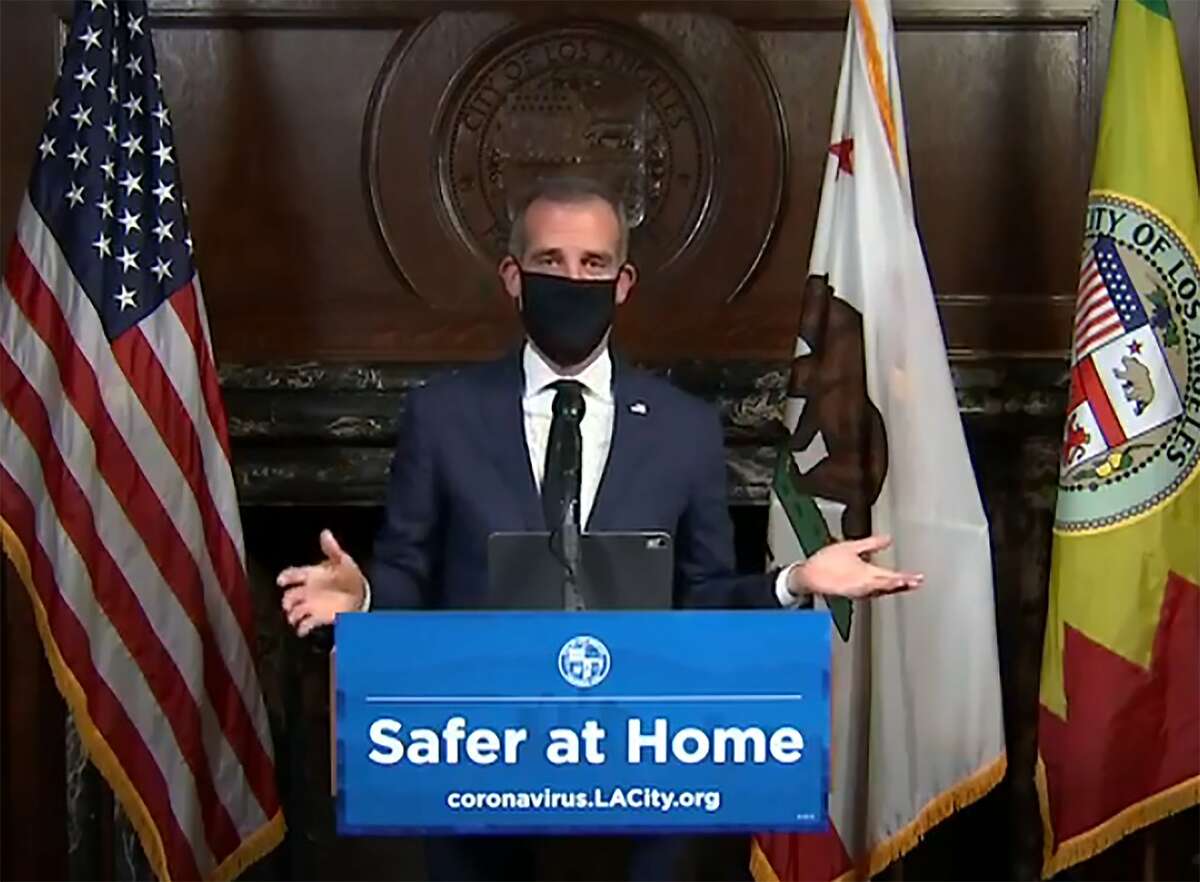 This still image taken from a live stream provided by Office of Mayor Eric Garcetti shows Los Angeles Mayor Garcetti displaying putting on a protective face mask during his daily news conference in Los Angeles on Wednesday, April 1, 2020. or Eric Garcetti via AP)