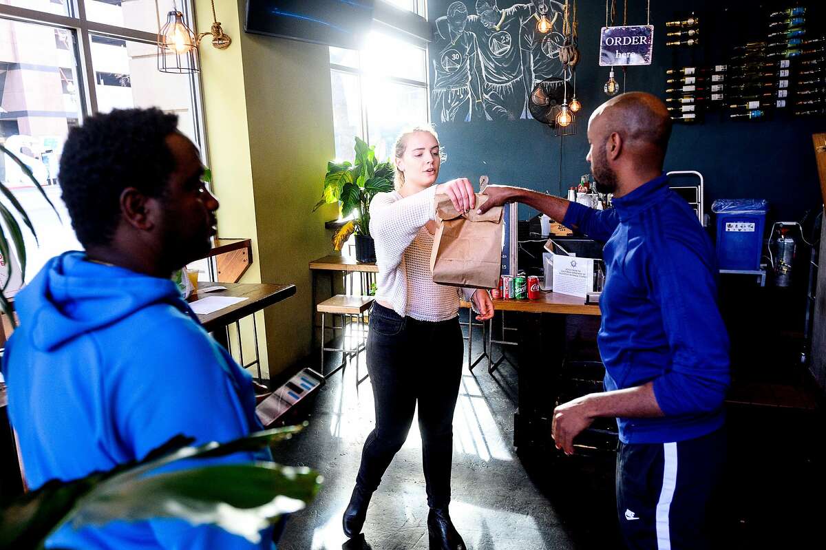 Sarah Holt-Gosselin hands an order to a delivery driver at alaMar on Friday, March 27, 2020, in Oakland, Calif. The restaurant has seen business increase as customers seek take-out and delivery options under coronavirus stay-at-home orders.