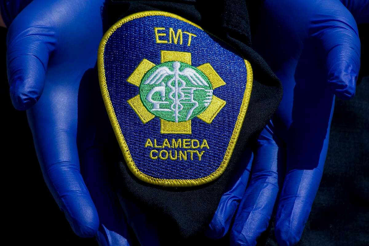 An Alameda County EMT wears gloves while holding their EMT patch on their work shirt while posing for a portrait at an undisclosed location in the Bay Area, Calif. Thursday, April 2, 2020. Alameda County EMTs and paramedics have been sidelined because of sickness or exposure to COVID-19. Many are not offered any additional paid time off and in many cases haven't accrued enough of their own vacation or sick days to be paid.
