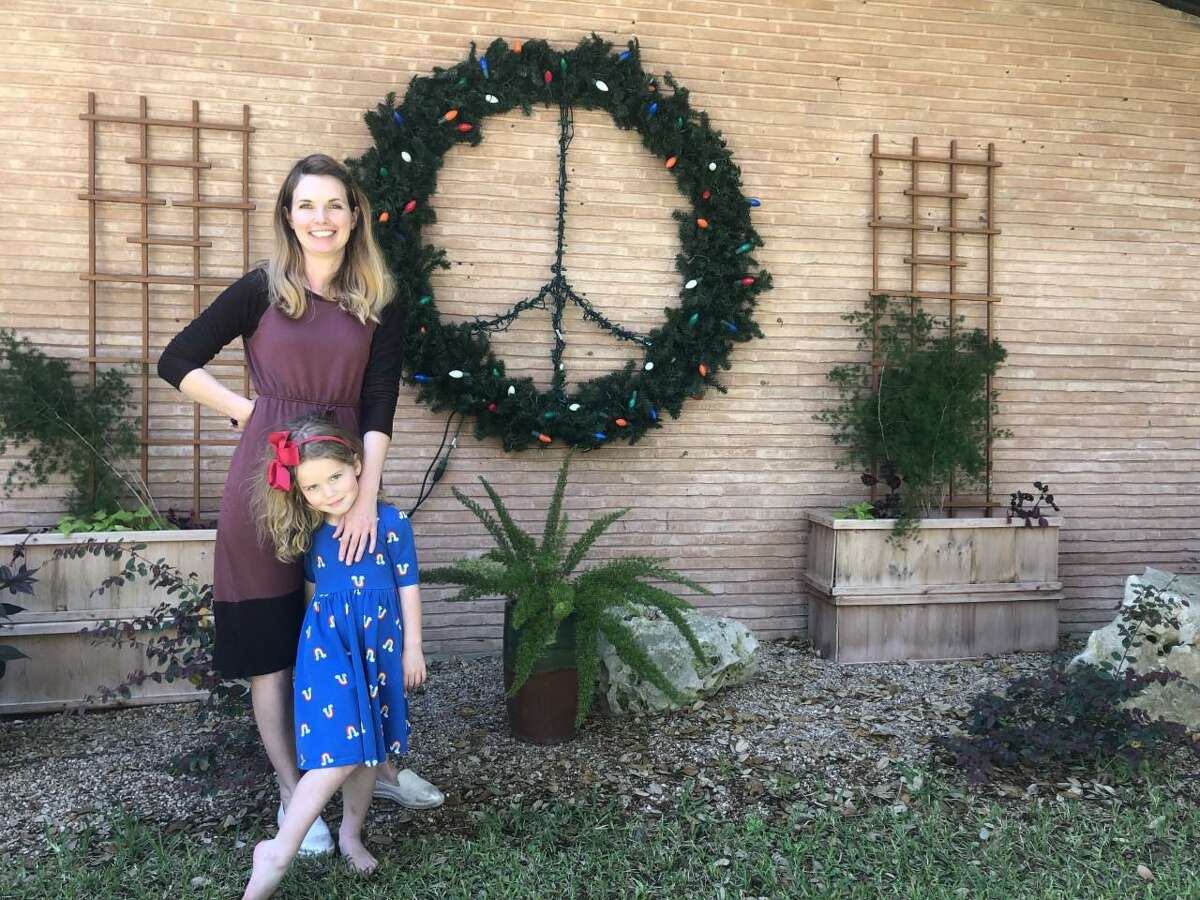Maggie Arnold and daughter Rose, 4, pose in front of a Christmas wreath, complete with an added peace sign, they recently hung in front of their Northwood home. Arnold said she wanted to spread some cheer during these trying times of the COVID-19 pandemic.