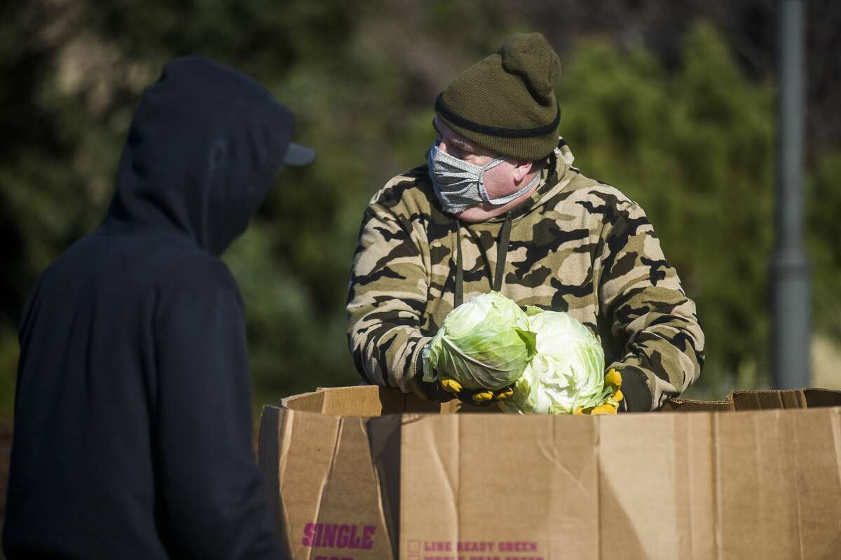Mike Kewell hands out heads of cabbage to other volunteers during a mobile food pantry hosted by Midland County Emergency Food Pantry Network Friday, April 3, 2020 at Dow Diamond in Midland. The Food Bank of Eastern Michigan provided a semi-truck filled with about 15,000-20,000 pounds of food for the event. (Katy Kildee/kkildee@mdn.net)