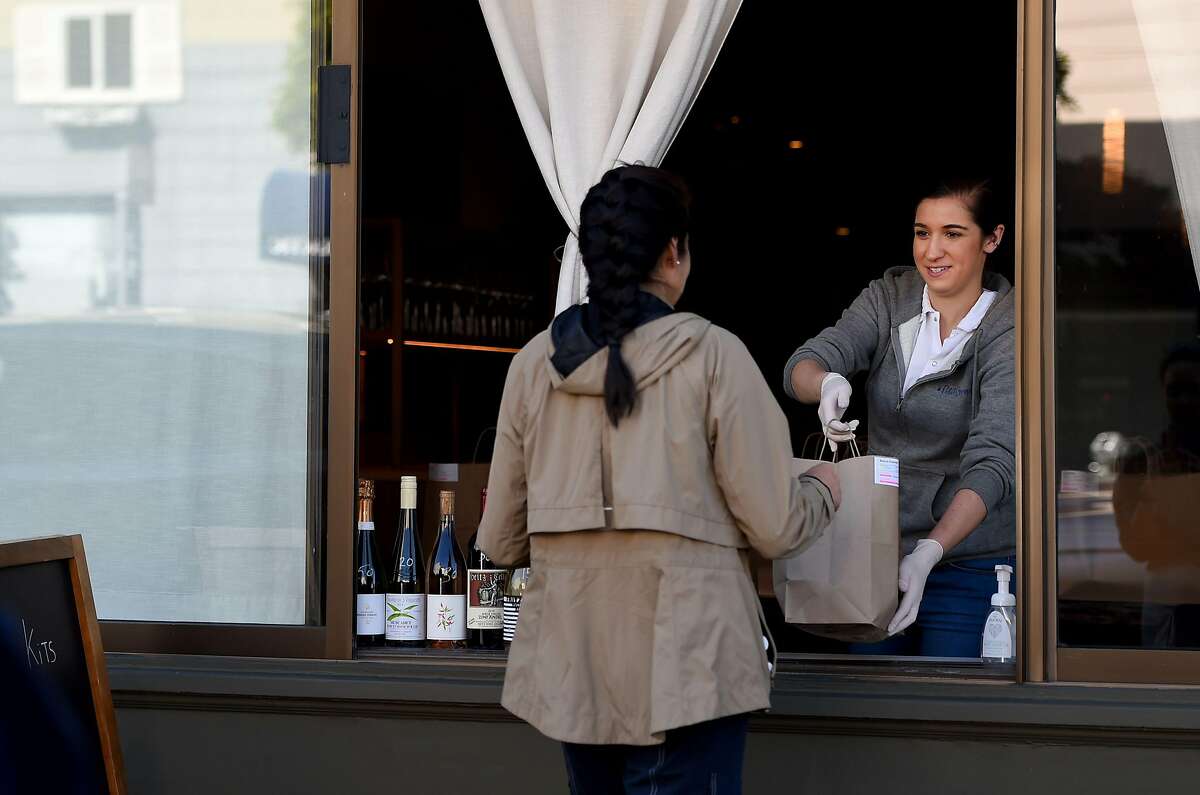 An employee for Atelier Crenn restaurant hands a takeout order to a customer through a window in San Francisco, California on April, 1, 2020, during the novel coronavirus outbreak. - The US death toll from the coronavirus pandemic topped 5,000 late on April 1, according to a running tally from Johns Hopkins University. (Photo by Josh Edelson / AFP) (Photo by JOSH EDELSON/AFP via Getty Images)