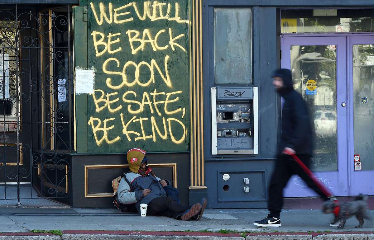 A man walks his dog past a homeless man sleeping under a message painted on a boarded up shop in San Francisco, California on April, 1, 2020, during the novel coronavirus outbreak. - The US death toll from the coronavirus pandemic topped 5,000 late on April 1, according to a running tally from Johns Hopkins University. (Photo by Josh Edelson / AFP) (Photo by JOSH EDELSON/AFP via Getty Images)