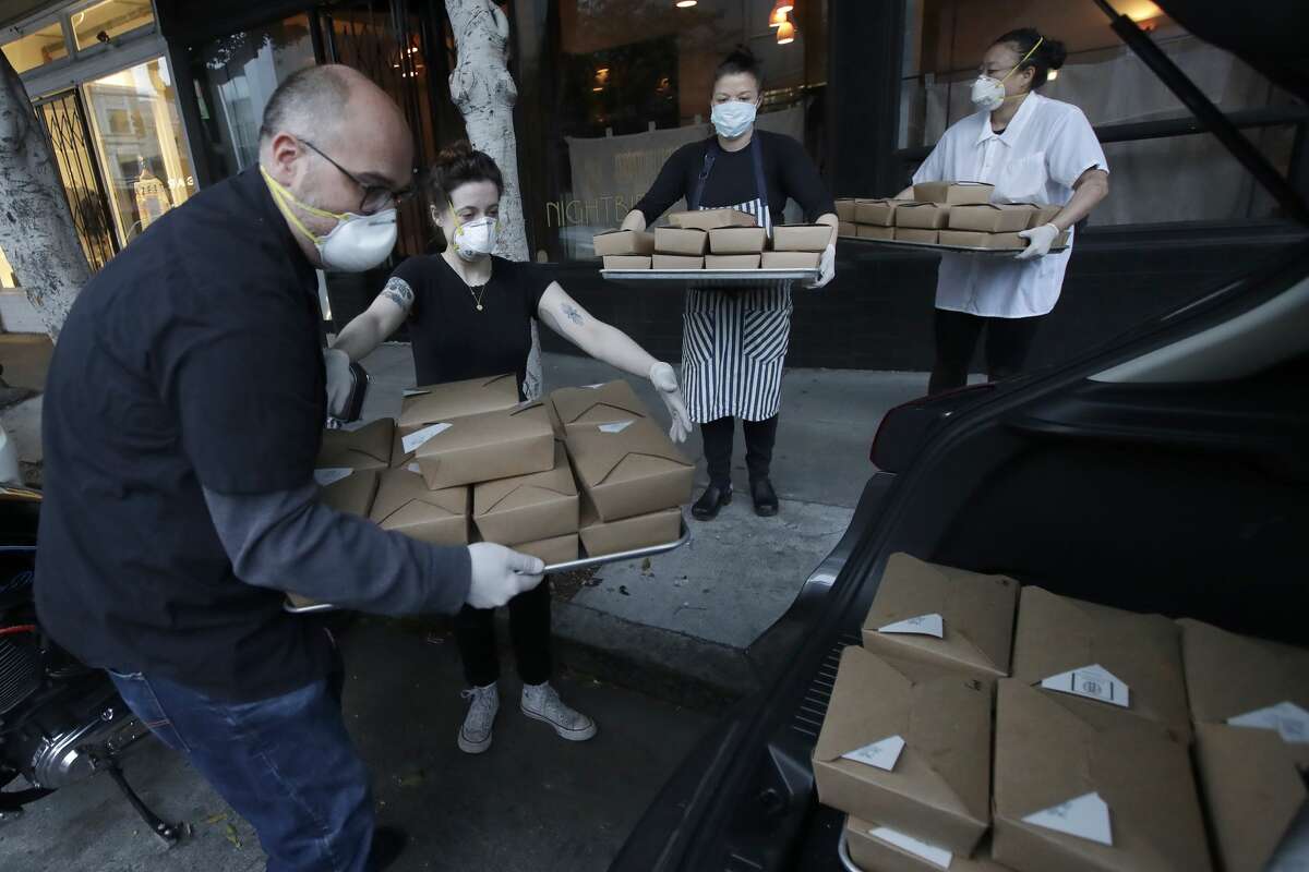 In this Friday, March 27, 2020, photo, Nightbird Restaurant general manager Ron Boyd, from left, pastry chef Hope Waggoner, chef and owner Kim Alter and sous chef Bailey Walton pack dinner boxes into Alter's car that were delivered to hospital workers in San Francisco. A group of tech-savvy, entrepreneurial San Francisco friends wanted to help two groups devastated by the coronavirus pandemic. They came up with a plan that involved soliciting donations, tapping friends in the restaurant world and getting San Francisco hospitals to accept free food cooked up by some of the city's top chefs.