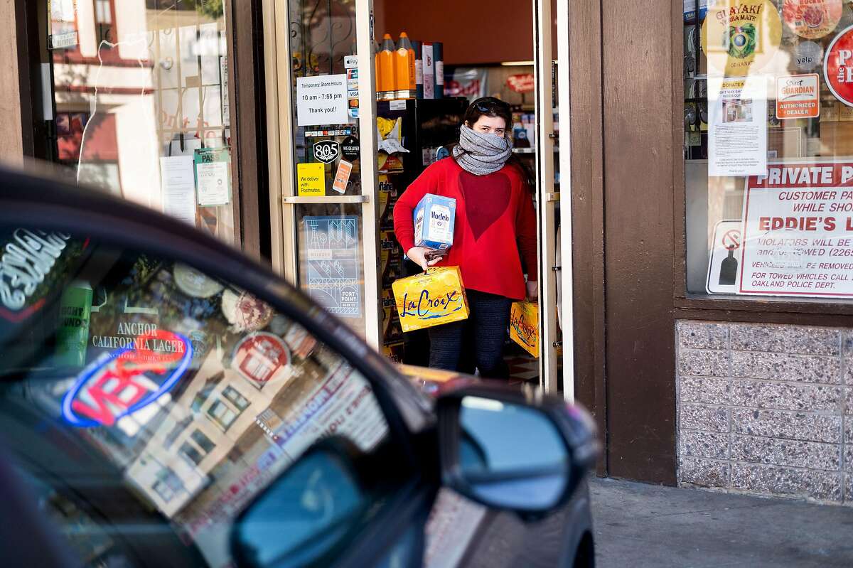 Anne Butterfield carries beer and sparkling water drinks during a shopping trip to Eddie's Drive In Liquors in Oakland, Calif., on Friday, April 3, 2020. The store maintains brisk business despite shelter-in-place orders enacted to slow the spread of coronavirus.