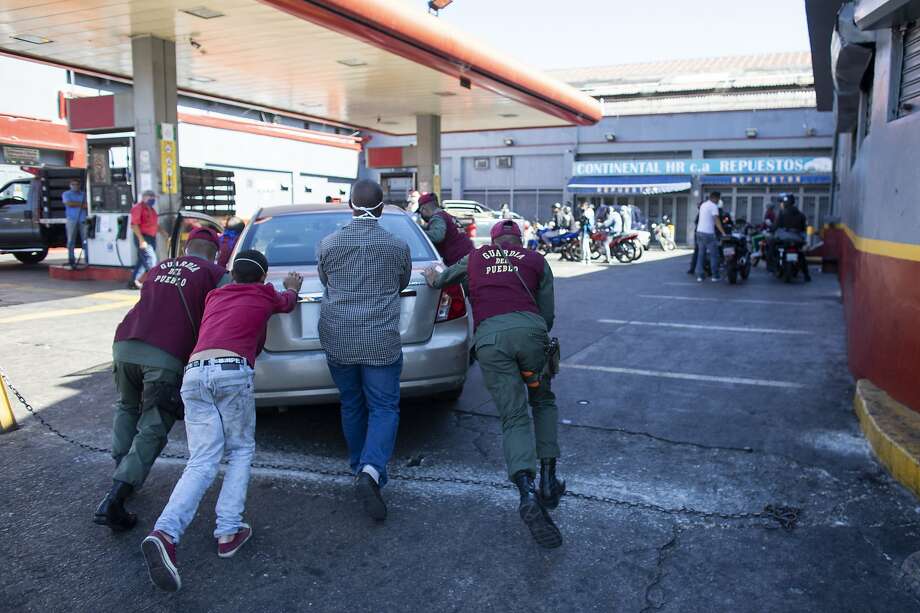 Bolivarian National Guard members help push a car into the gas station during the second week of the national quarantine on March 27, 2020 in Caracas, Venezuela. Photo: Leonardo Fernandez Viloria / Getty Images