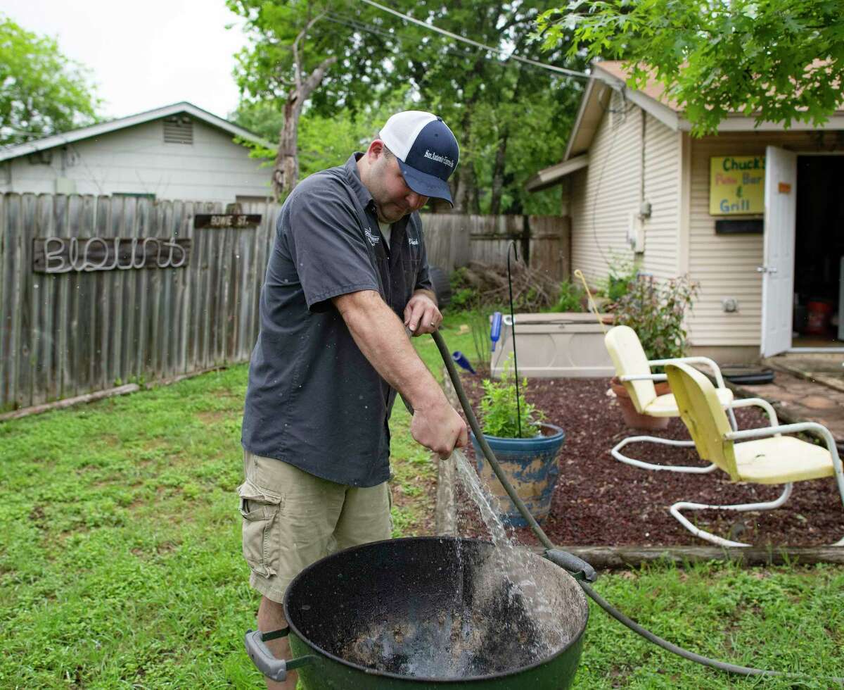 Chuck Blount washes down the base of his grill with a garden hose. Removing caked ash and grease regularly is a good way to extend the life of the grill, provided it’s quickly dried with a towel.