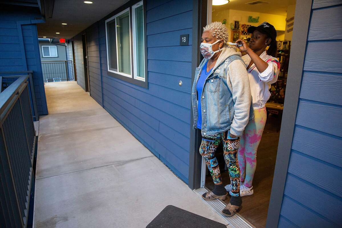 From left: Vicky Blake gets help from her niece Curtisha Bell to tie her surgical mask on Friday, April 3, 2020, in Redwood City, Calif. Amid the coronavirus pandemic and shelter-in-place orders, Blake celebrated her 62nd birthday at home with family and friends chatting with her through Facebook Live. Blake and her niece made festive surgical masks to celebrate.