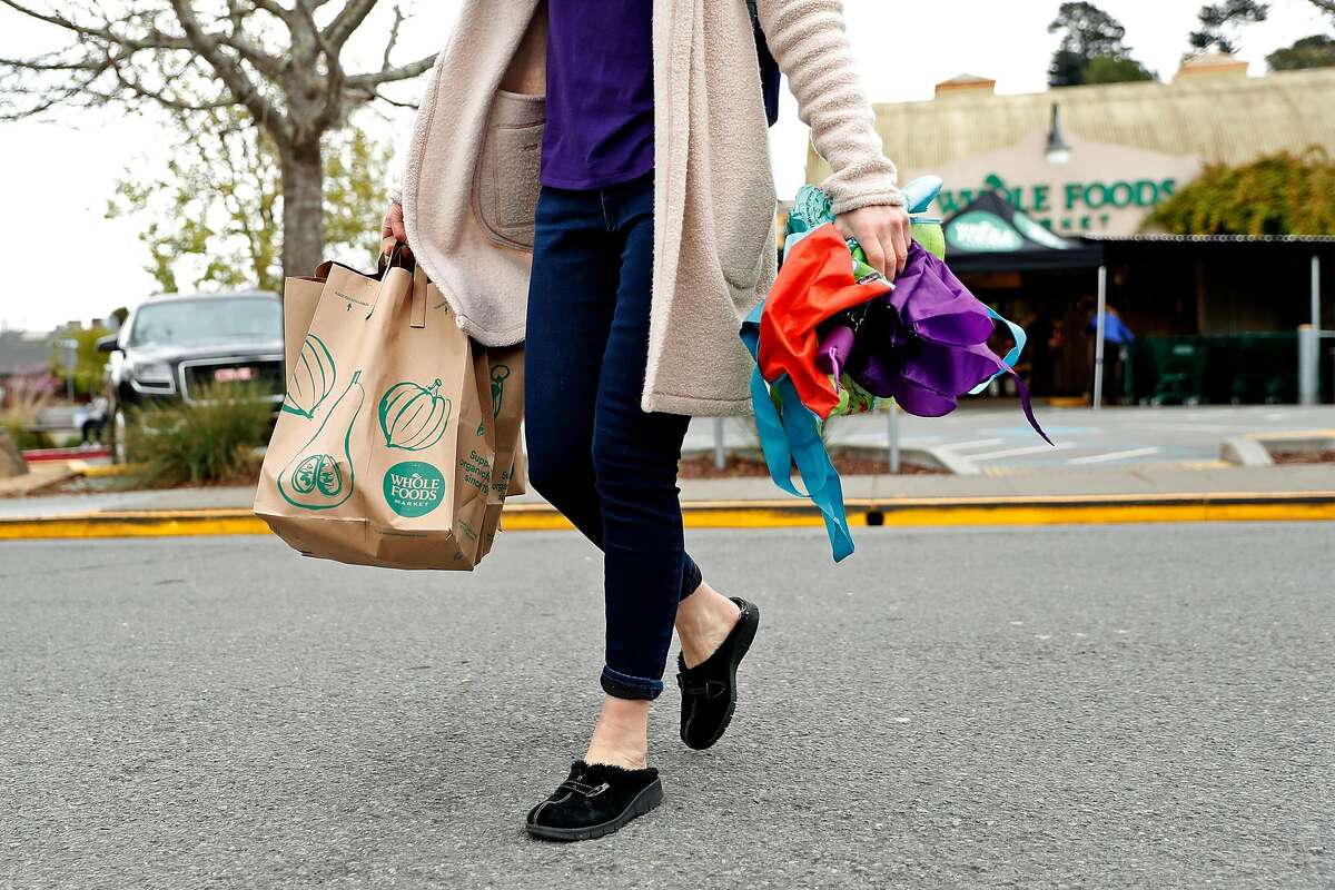 After not being able to use her own bags, a shopper walks across Evergreen Avenue after shopping at Whole Foods in Mill Valley, Calif., on Monday, April 6, 2020.