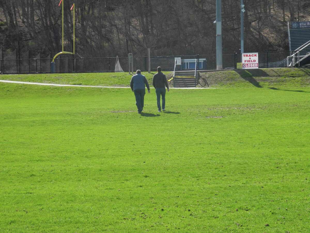 Two men walk across a field at Wilton High School toward the path that leads to Cider Mill School. People caught using closed recreational facilities face a $92 trespassing fine.