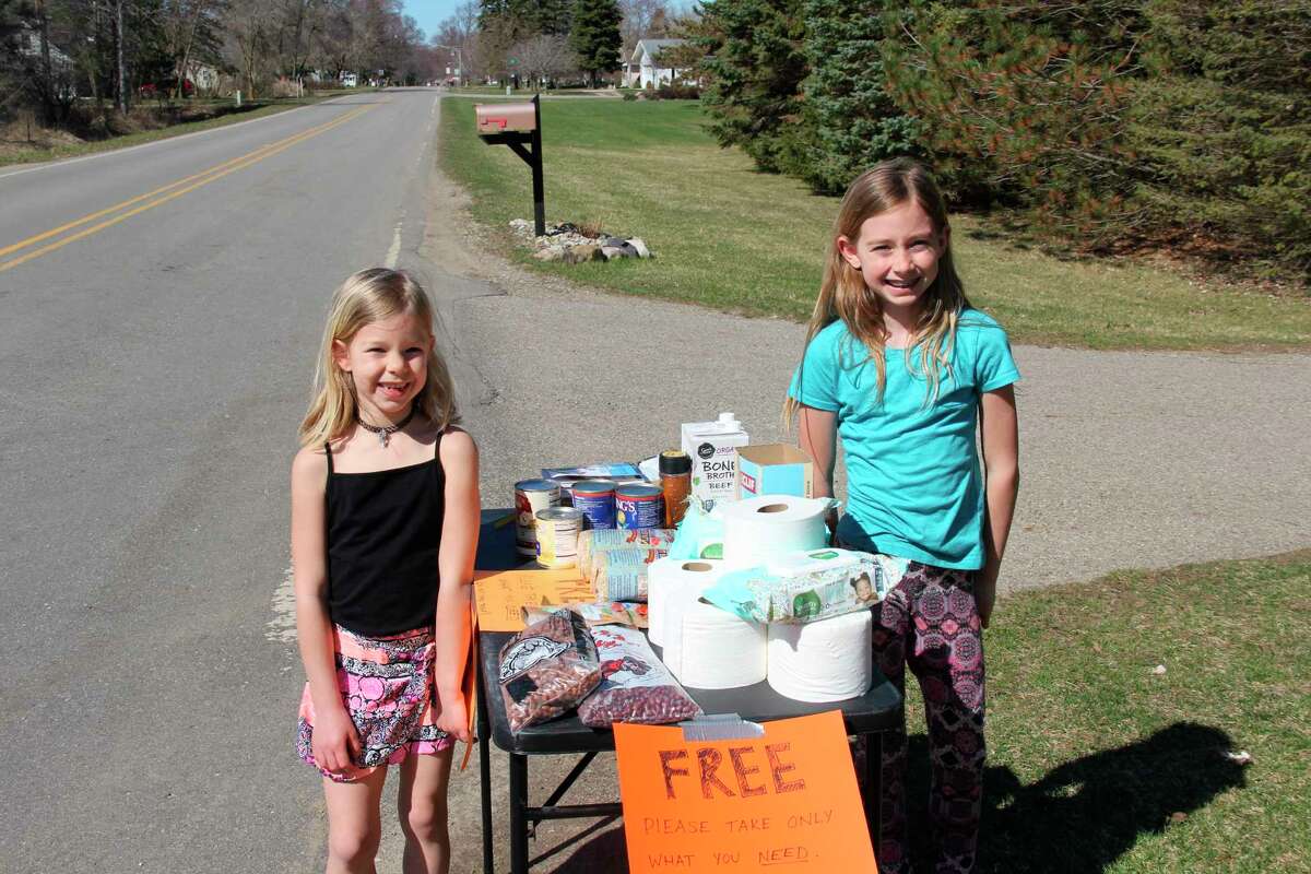 Selah and Rhiana Leipprandt, ages 6 and 9 respectively, stand by their table stand of free supplies on South Silver Street in Bad Axe recently. Their parents, Rachel and Tyler, came up with the idea to try and help whoever they can without making direct contact. (Robert Creenan/Huron Daily Tribune)