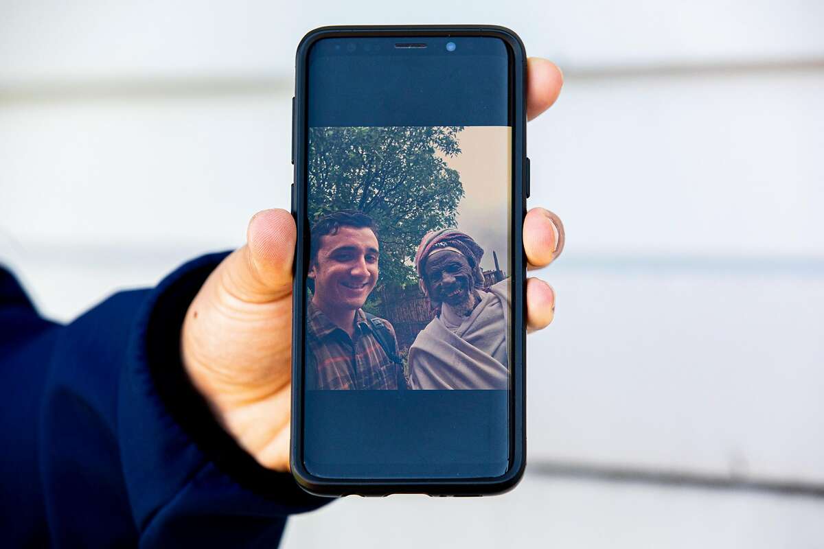 Eddy Holman shares a photo of him and town elder Father Maachaa displayed on his phone while in San Lorenzo, Calif. Tuesday, April 7, 2020. Eddy was a PeaceCorps volunteer in Ethiopia who was evacuated from the country because of COVID-19. He's staying at the home of his mother's boyfriend and using her cell phone as resettles into life in the Bay Area and waits for the program to resume.