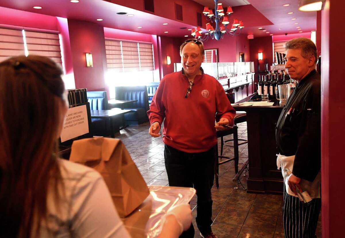 From left; Jacqueline Silano brings a takeout order to Dan Solaz, of Trumbull, as owner Ralph Solano looks on at Ralph ‘n’ Rich’s restaurant in Bridgeport, Conn. on Tuesday, April 7, 2020. Bridgeport Mayor Joe Ganim has ordered city businesses to close at 8 pm in the wake of the coronavirus pandemic.