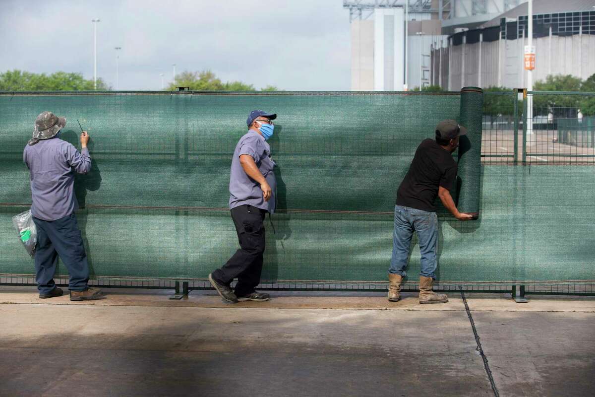 Workers cover fences while setting up a makeshift field hospital at NRG Park in preparation for an expected surge of COVID-19 patients in Harris County Tuesday, April 7, 2020, at Orange Lot in Houston.