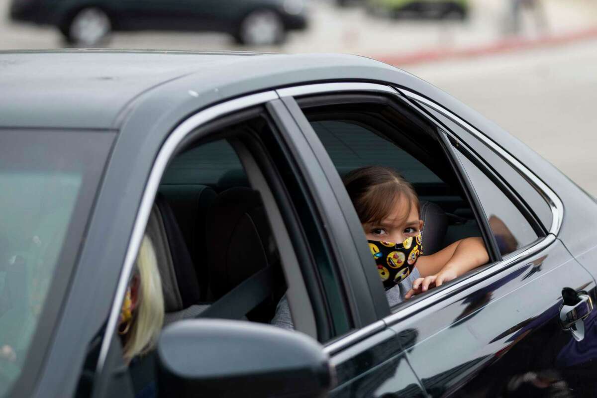 A young girl peers out the window of her vehicle while wearing an emoji pattern mask during the San Antonio Food Bank drive-through food distribution event April 7, 2020 in the Toyota Field parking lot in San Antonio. Mayor Ron Nirenberg and County Judge Nelson Wolff are urging San Antonio area residents to continue wearing masks and maintaining a 6-foot social distance from others when out in public to prevent a resurgence of the deadly novel coronavirus.