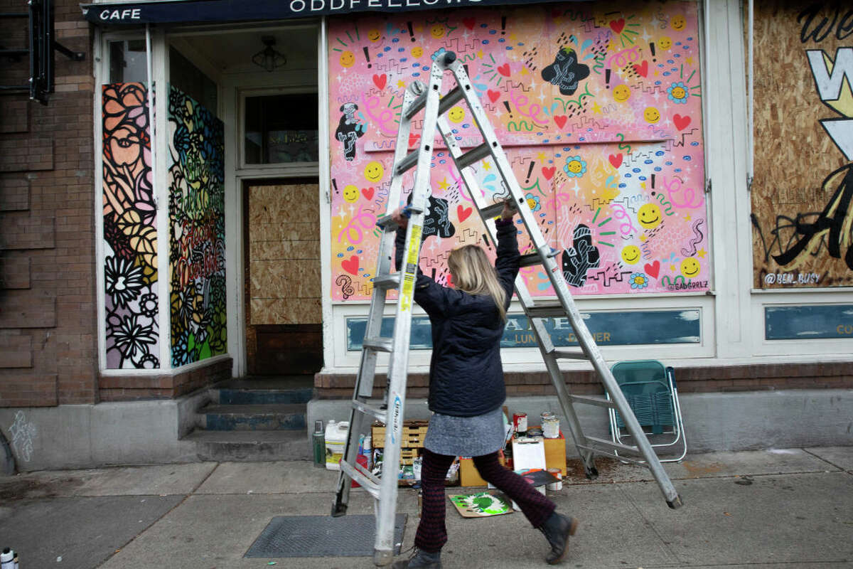 SEATTLE, WA - MARCH 24: Artist Josephine Rice paints a mural in the boarded up doorway of Oddfellows Cafe and Bar on March 24, 2020 in Seattle, Washington. Click through the slideshow to see before and after photos of popular and frequented places across the Seattle area amid the novel coronavirus outbreak. >>>  