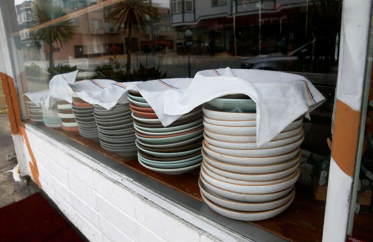 Dishes normally used for dining room service is stacked on the window sill while Cassava restaurant serves take-out orders only on Balboa Street in San Francisco, Calif. on Wednesday, April 8, 2020. Cassava owners have had some of their small business insurance claims denied as the restaurant struggles to stay open by serving take-out orders only during the coronavirus pandemic.