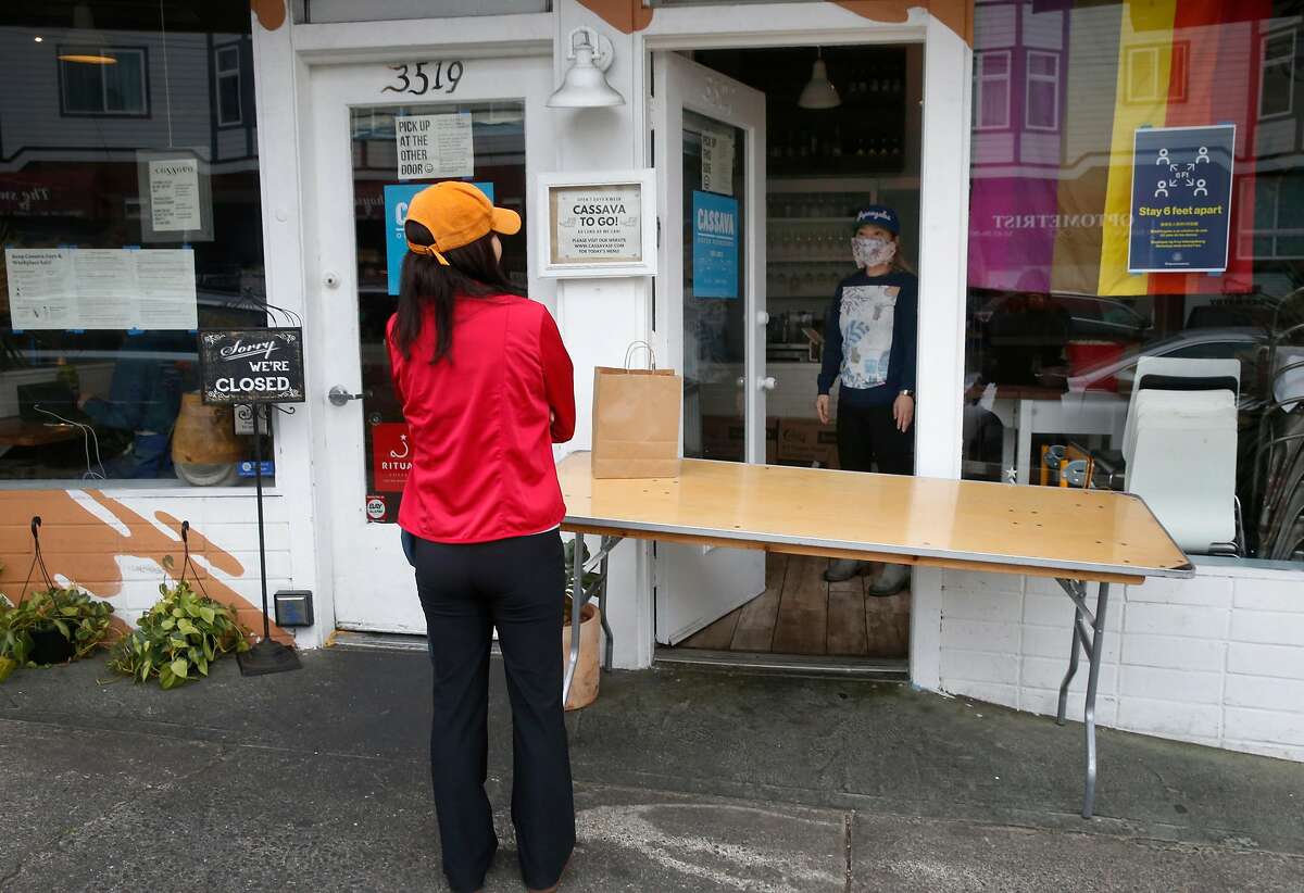Cassava restaurant co-owner Yuka Ioroi (right) greets a customer picking up a to-go order in San Francisco, Calif. on Wednesday, April 8, 2020. Cassava owners have had some of their small business insurance claims denied as the restaurant struggles to stay open by serving take-out orders only during the coronavirus pandemic.