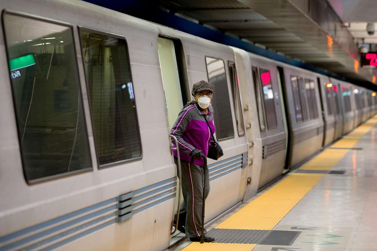A woman wears a face mask while using a cane to exit a train at 19th Street BART Station in Oakland, Calif. Friday, April 3, 2020. Although BART has seen a drastic decline in ridership, those who still use their services have been seen wearing protective gear and practicing social distancing.