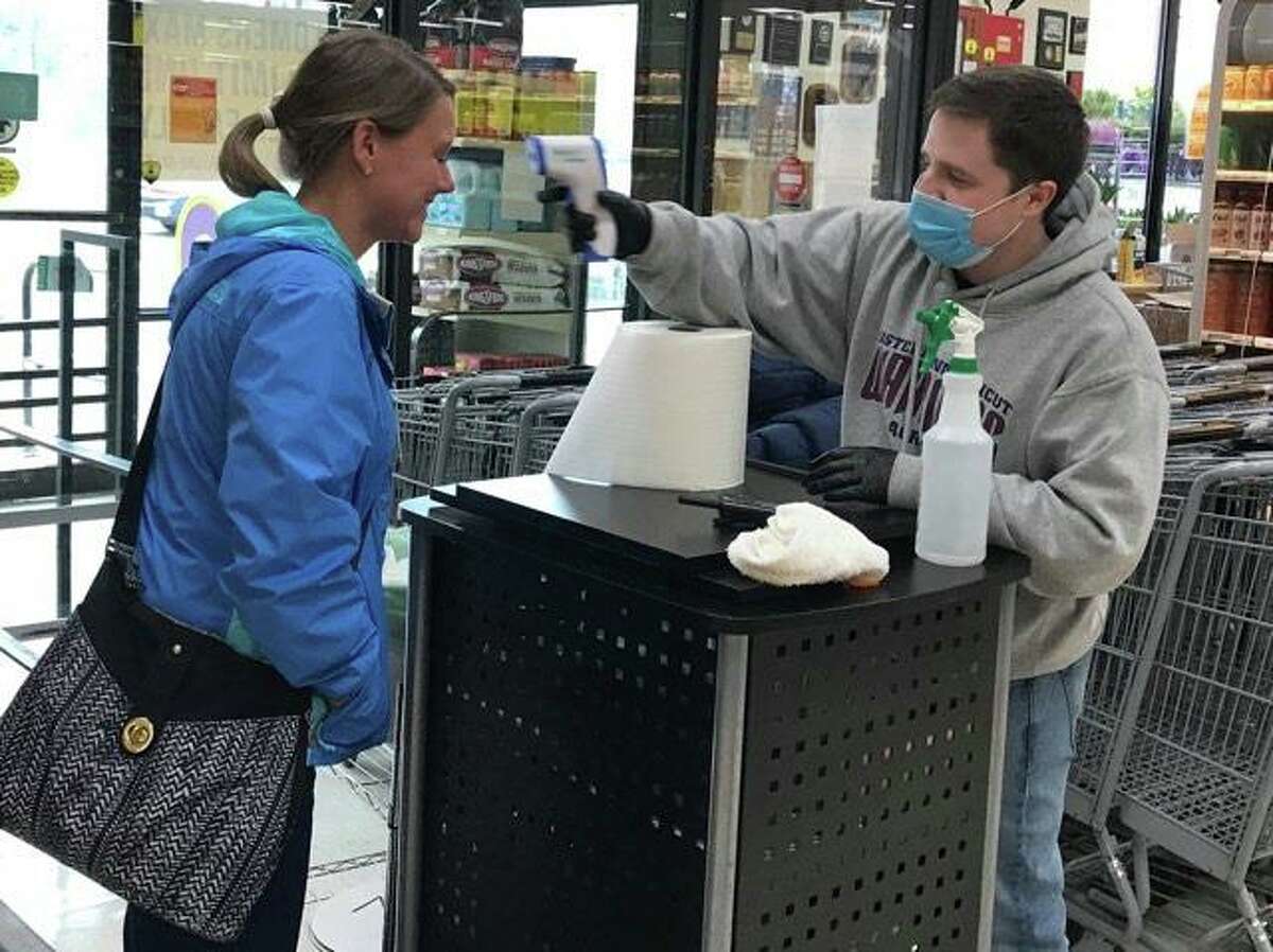 Wes Thompson, an employee at LaBonne’s Market in Prospect, uses a temporal thermometer to take the temperature of Becky Lacilla before she was allowed to shop at the store Wednesday.