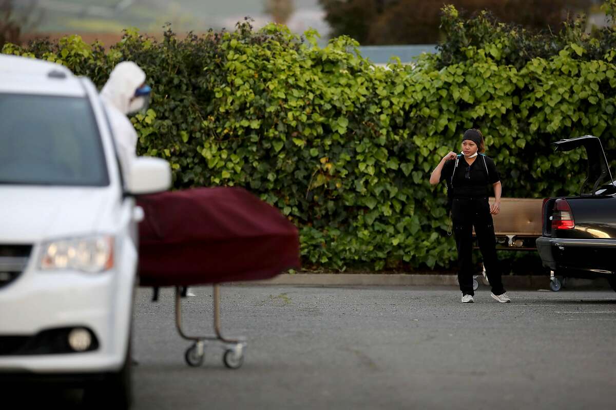 An employee looks on as a body is being prepared for being loaded into a van at Gateway Care & Rehabilitation in Hayward.