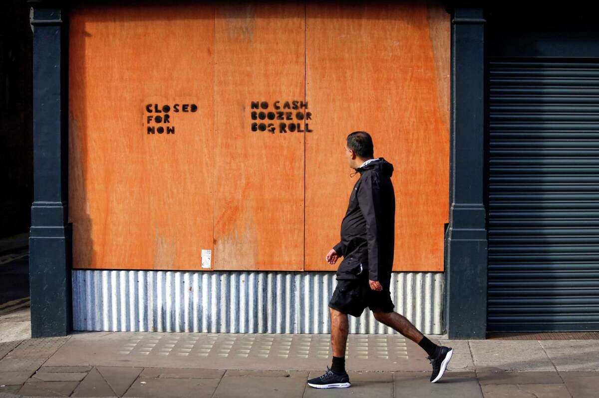 A pedestrian passes a boarded up window at a bar in Manchester, England, on April 8, 2020.