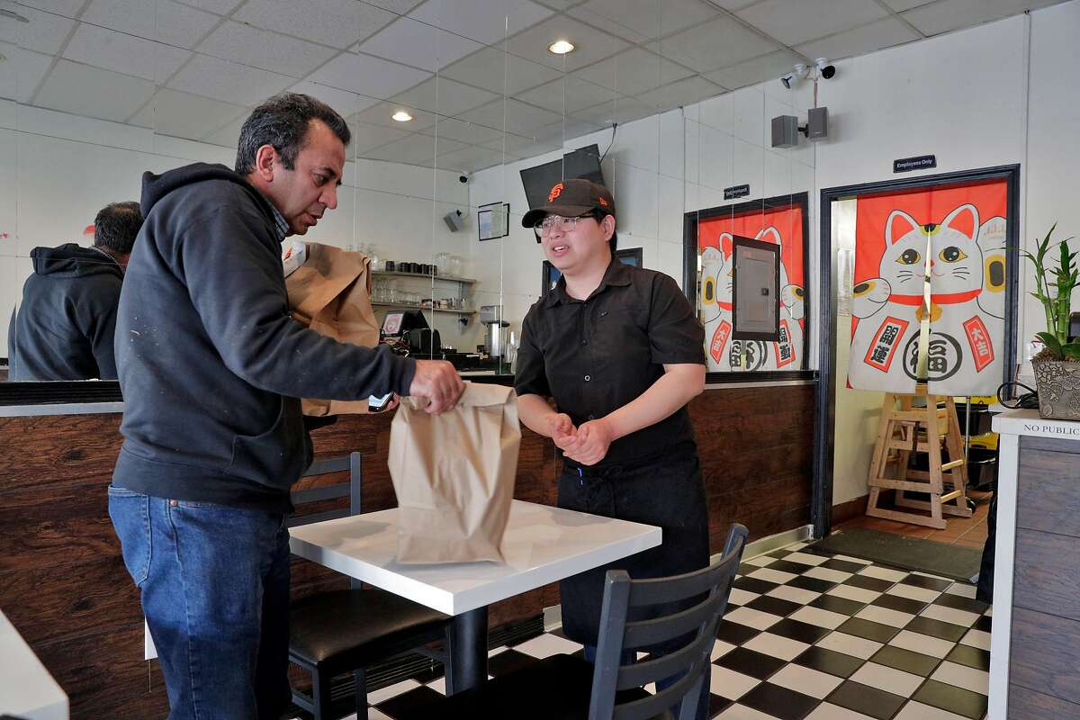 Wathanyu Sae-Kang give a delivery order to driver Fawzi Hameedat, left, at Dozo Ramen restaurant in Oakland, Calif., on Tuesday, March 17, 2020 as residents take advantage of open restaurants for take-out and delivery orders after being told to shelter in place to curtail the spread of the Covid-19 virus in the 6 Bay Area counties.