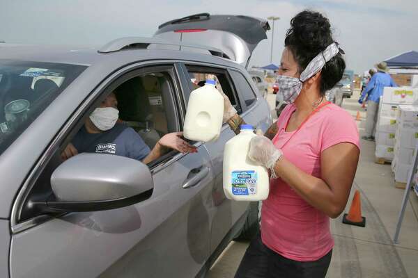 Heather Martinez greets and hands over two gallons of milk as thousands of people in cars - some waiting since late yesterday afternoon - gather at Traders Village to get food from the San Antonio Food Bank on Thursday, Apr. 9, 2020.