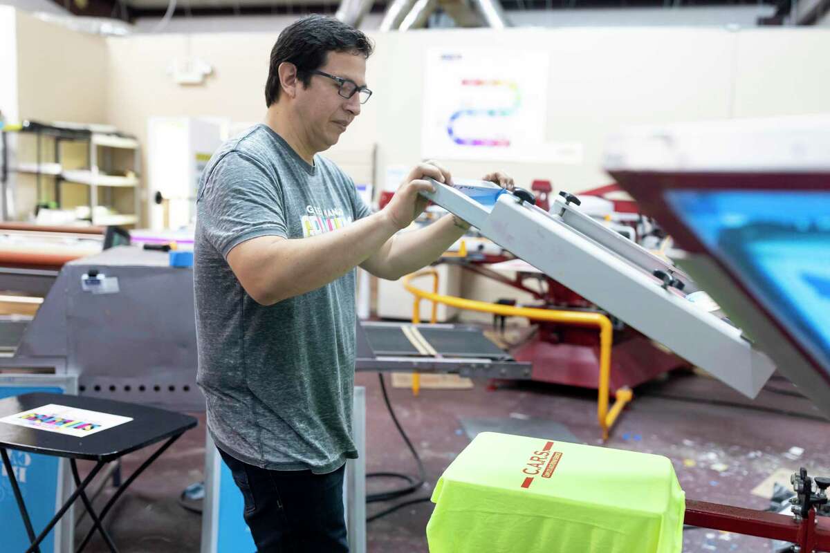 Rocky Castillo, owner of Green Mango Graphics in Conroe, demonstrates the screen printing process, Thursday, April 9, 2020.Proceeds from their initiative to assist local businesses will be evenly disbursed between the local business and Green Mango Graphics.