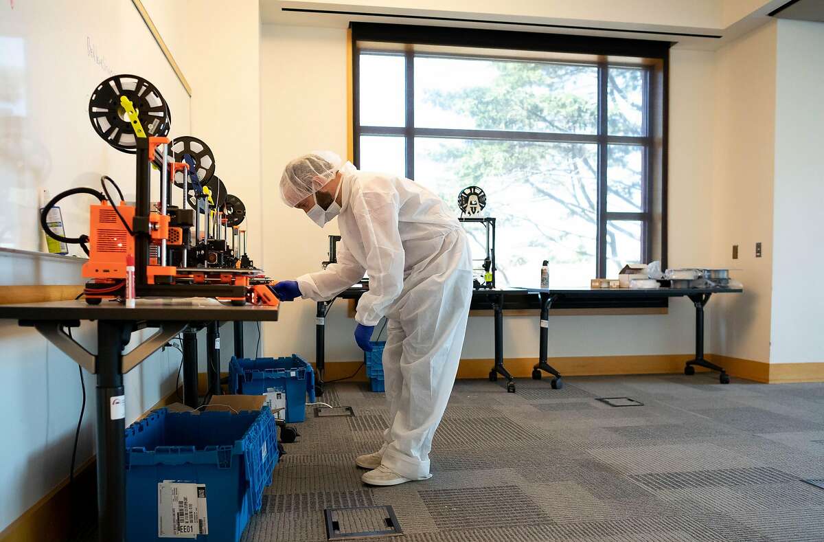 Dylan Romero, Makers Lab manager, checks on 3D prints of PLA filament headbands, part of a medical face shield his team is mass producing to offset shortages during the Coronavirus pandemic, at the Kalmanovitz Library, at the Parnassus campus.