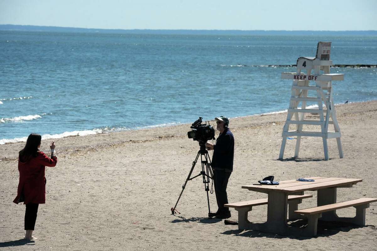 A television news reporter and photographer broadcast from a vacant Penfield Beach, in Fairfield, Conn. April 6, 2020. The beach was clear of people Monday afternoon. Town of Fairfield beaches and parks are currently closed to the public due to coronavirus precautions.