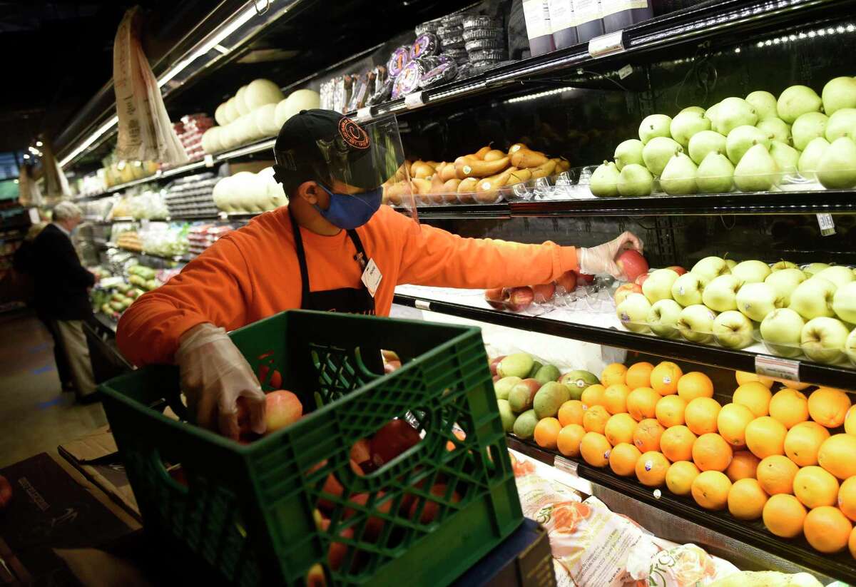 Citarella employee Hovie Pandong stocks the shelves with apples while wearing a mask and gloves at Citarella Gourmet Market in Greenwich, Conn. Thursday, April 9, 2020. As an extra measure to prevent the spread of coronavirus, Greenwich is mandating food service workers to wear a protective mask and gloves at work.