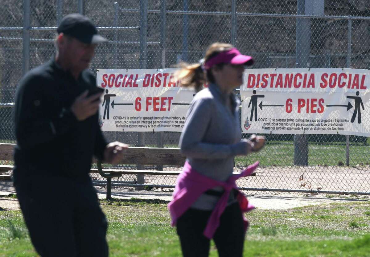 Joggers run laps as a sign promoting social distancing is displayed behind them on a fence at Scalzi Park in Stamford, Conn. Monday, April 6, 2020. Doctors recommend keeping a distance of at least six feet away from others to reduce the risk of contracting the coronavirus.