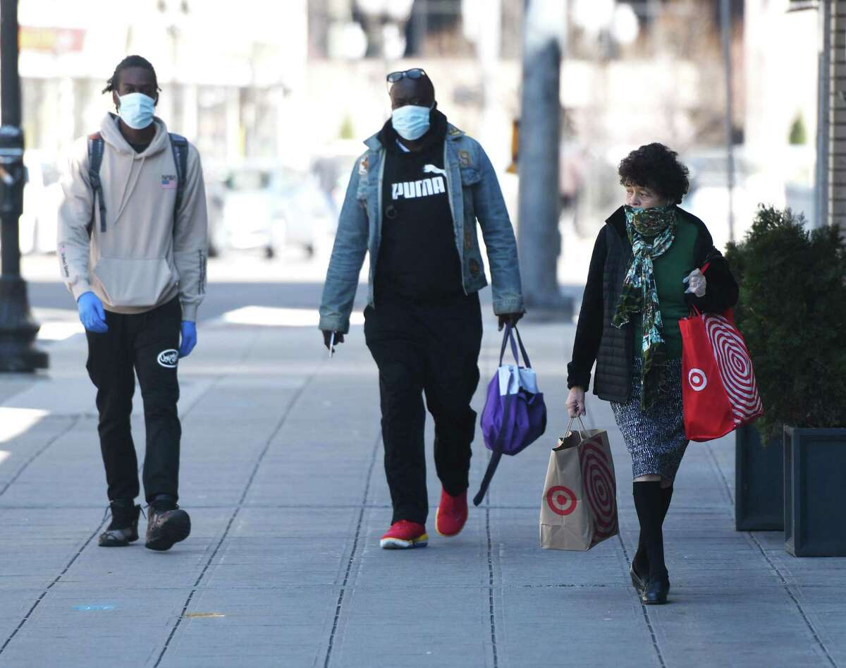 A woman covers her nose and mouth with a scarf while two men wear surgical masks to prevent the spread of coronavirus in Stamford, Conn. Monday, April 6, 2020.