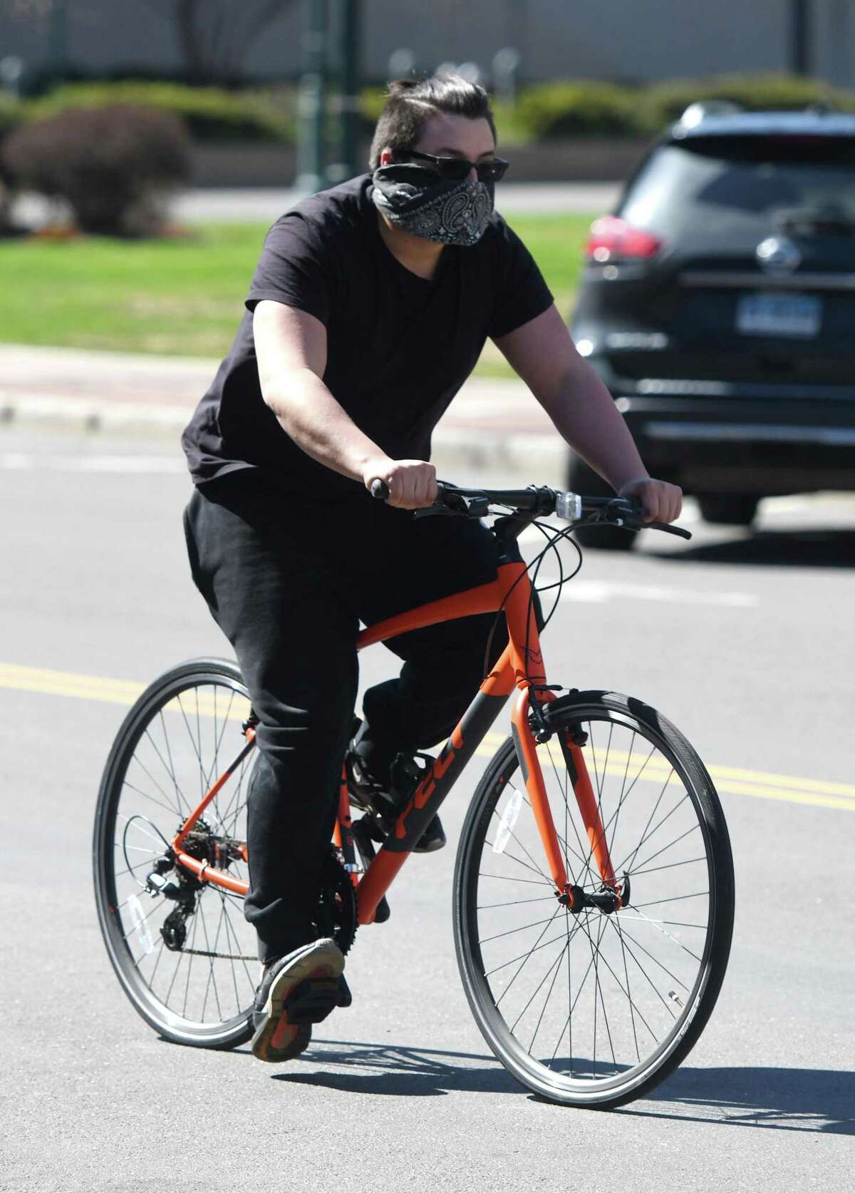 A man shields his nose and mouth with a bandana while riding through downtown Stamford, Conn. Monday, April 6, 2020.