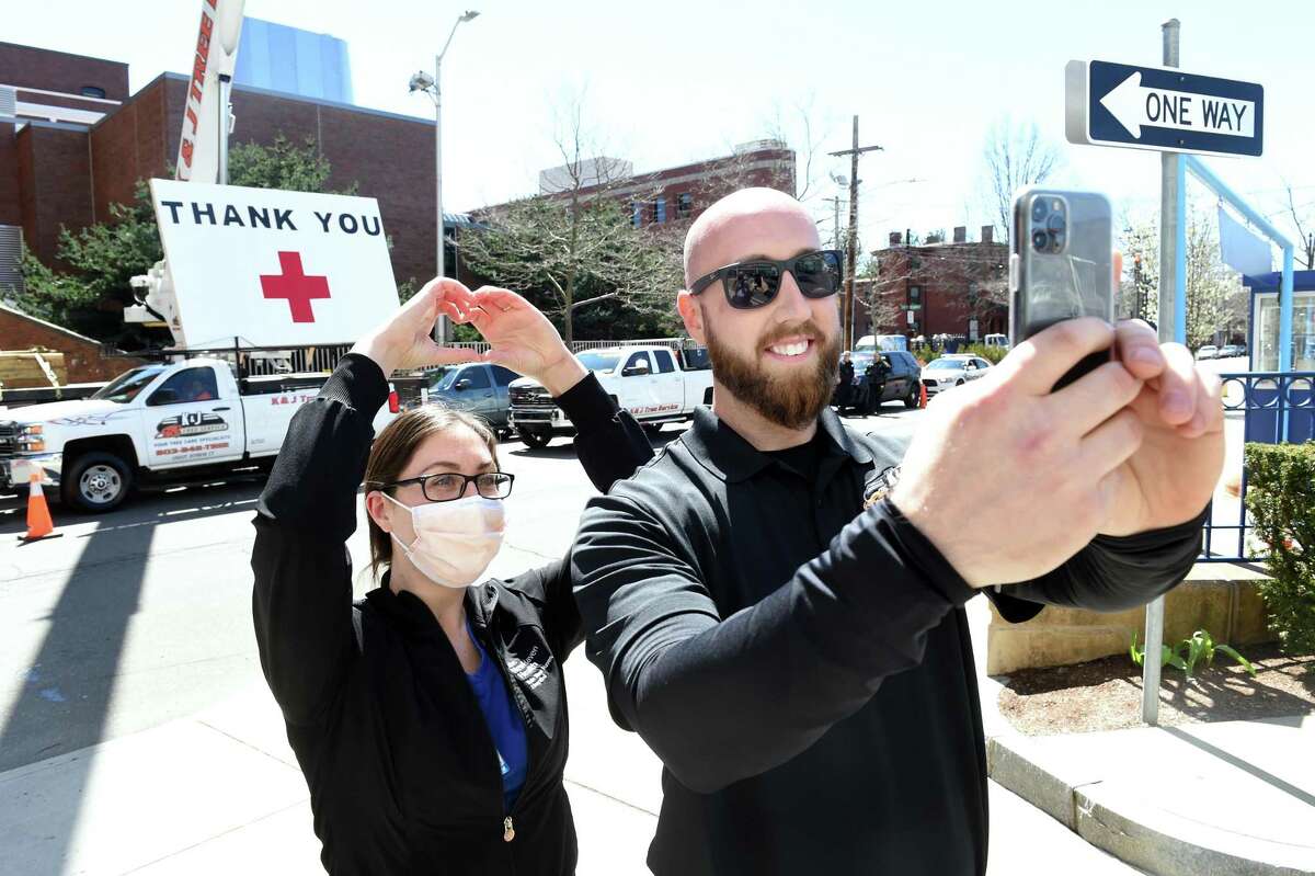 Registered Nurse Jillian Wright makes a heart sign with her hands while taking a selfie with her brother, Kyle DeLucia, founder and owner of K&J Tree Service, in front of Yale New Haven Hospital on April 6, 2020. DeLucia put up a 50 foot United States flag and a large thank you across from the hospital on York Street to show his appreciation for the work of the hospital staff.