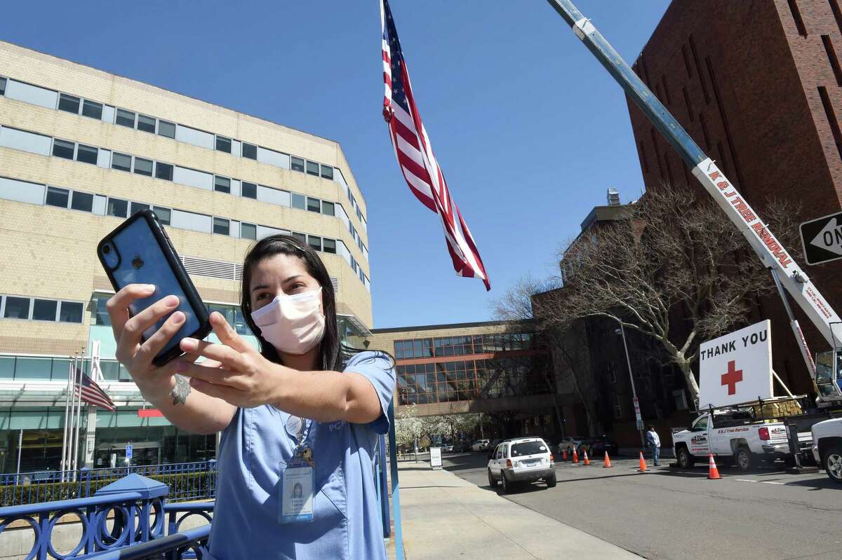 Patient Care Associate Ashlee Tarsia takes a selfie in front of a 50 foot United States flag and thank you put up by Kyle DeLucia, founder and owner of K&J Tree Service, in front of Yale New Haven Hospital on April 6, 2020. DeLucia put up the flag and a large thank you across from the hospital on York Street to show his appreciation for the work of the hospital staff.