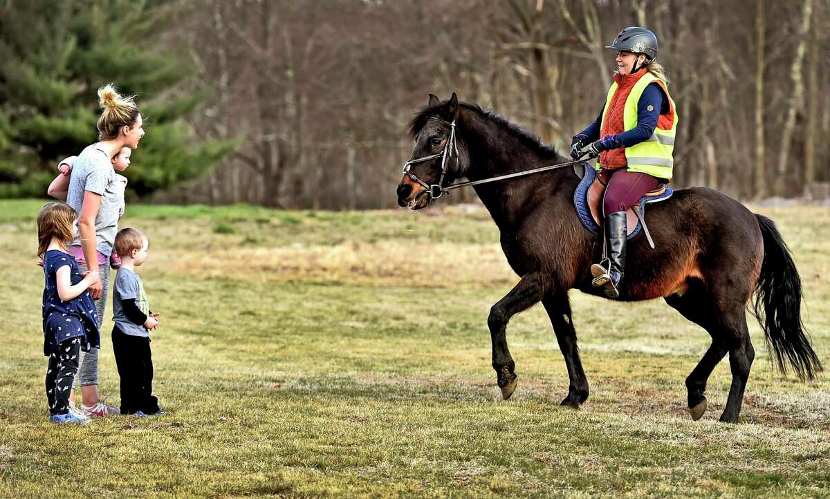 Bethany, Connecticut - Wednesday, April 01, 2020: Cory Sells of Woodbridge using her Paso Fino breed horse Torpedo, 19, show's of Torpedo's unique gait to Alissa Hill of Bethany and her children Madison, 1, Bradford, 3, and Mackenzie, 5, on Bear Hill Road in Bethany. Sells, using Torpedo as a therapy horse, ride around the Bear Hill Road area in Bethany twice a week, using social distancing, visiting neighborhood children and their parents quarantined in their homes during the COVID-19 / Coronavirus pandemic.