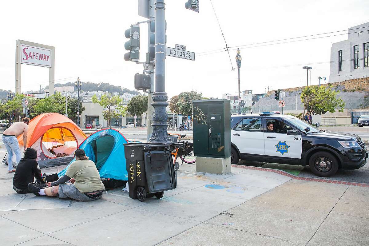 A San Francisco police officer asks a group of people experiencing homelessness to move six feet apart on April 9, 2020 on Dolores and Market Street.