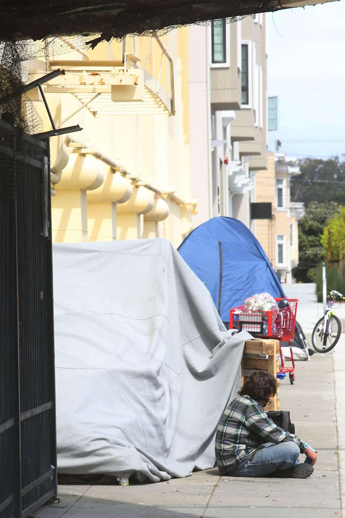 Luke Ellis of San Francisco sits on 18th Avenue next to tents and shelters as he rests while running an errand and visiting a friend on Thursday, April 9, 2020 in San Francisco, Calif. Ellis said he is not homeless but was visiting a friend.