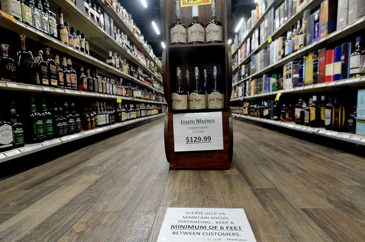 FILE — Signs placed throughout the Longhorn Liquor store encourage social distancing among customers and advises those with a cold or cough to remain outside. (Hearst)