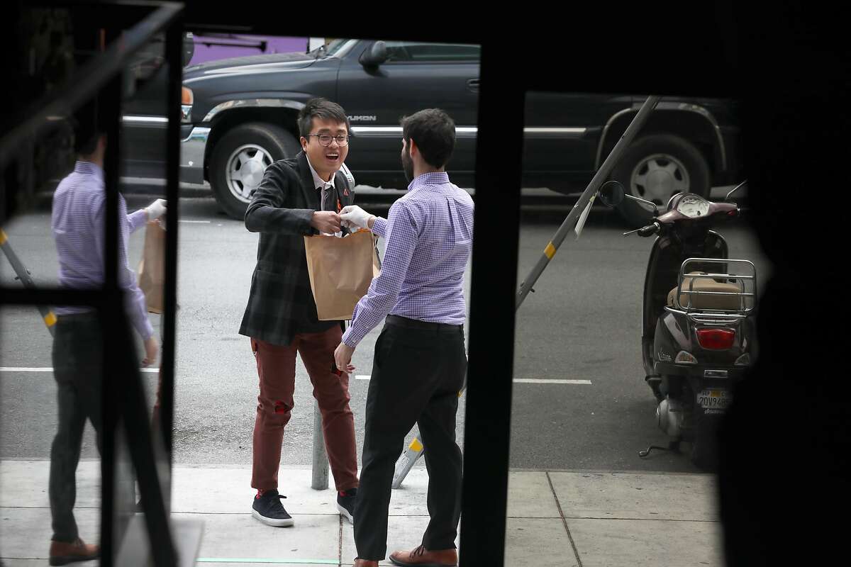 Stefan Fan (middle left) picks up sourdough bread and miso soup from general manager Gregory Saavedra in front of Lazy Bear restaurant in the Mission on Thursday, April 9, 2020, in San Francisco, Calif.